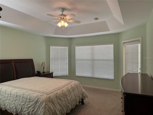 carpeted bedroom with ceiling fan and a raised ceiling