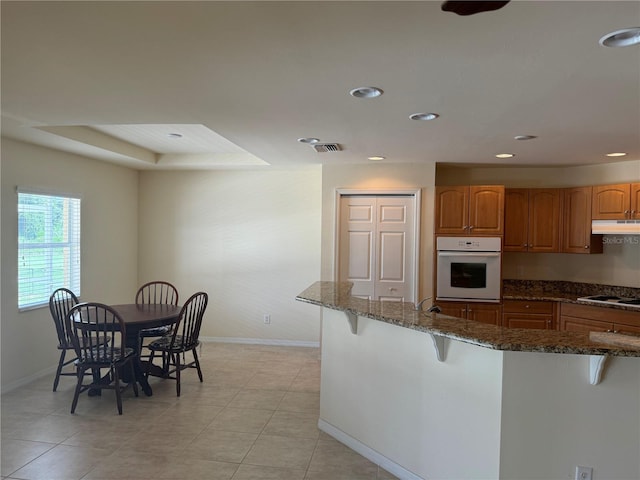 kitchen with a kitchen bar, white oven, dark stone counters, and light tile patterned floors