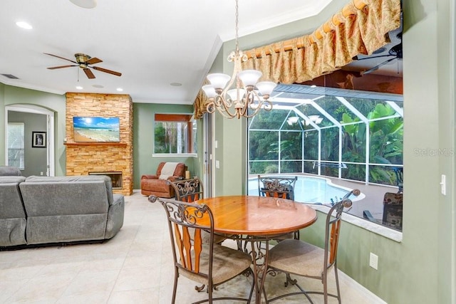 tiled dining area featuring ornamental molding, ceiling fan with notable chandelier, and a stone fireplace