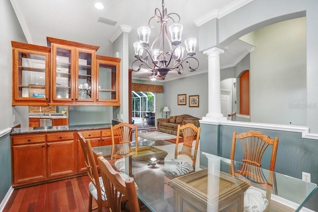 dining room featuring dark hardwood / wood-style flooring, crown molding, decorative columns, and a chandelier