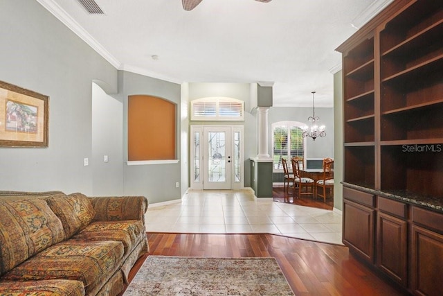 tiled living room featuring ornate columns, crown molding, and a notable chandelier