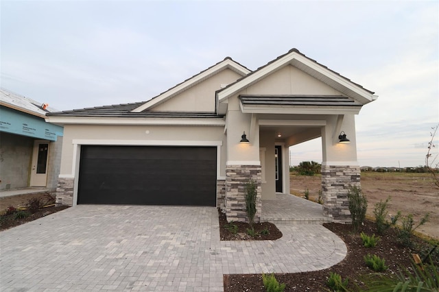 view of front of property featuring a garage, stone siding, decorative driveway, and stucco siding