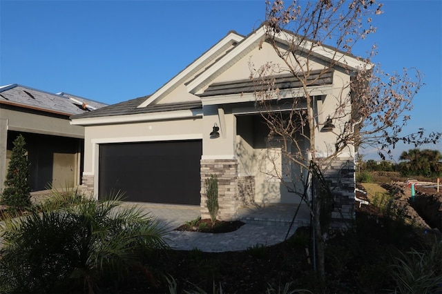 view of front facade featuring a garage, stone siding, decorative driveway, and stucco siding