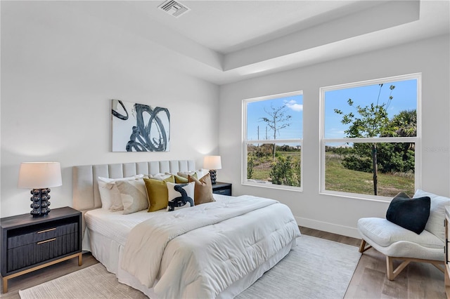 bedroom featuring a raised ceiling, visible vents, multiple windows, and wood finished floors