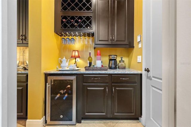 bar featuring light tile patterned floors, light stone countertops, wine cooler, and dark brown cabinetry