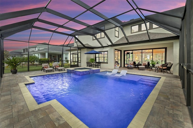 pool at dusk with an in ground hot tub, a patio, and glass enclosure