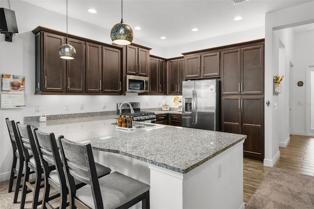 kitchen featuring kitchen peninsula, light stone countertops, appliances with stainless steel finishes, hardwood / wood-style flooring, and pendant lighting