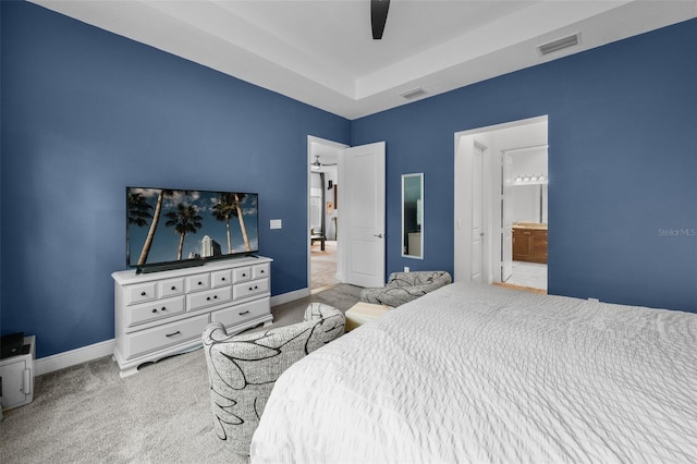 carpeted bedroom with a tray ceiling, ceiling fan, and ensuite bathroom