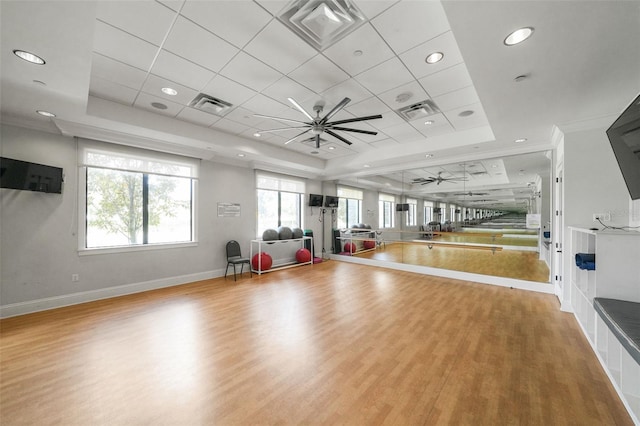 exercise area featuring crown molding, a tray ceiling, and light wood-type flooring