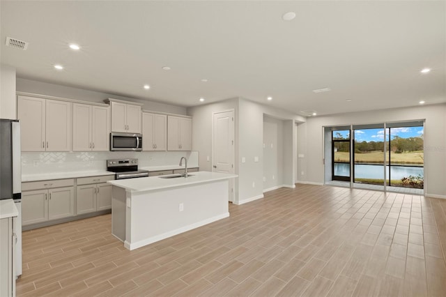 kitchen featuring sink, backsplash, stainless steel appliances, white cabinets, and a center island with sink