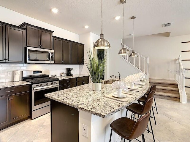 kitchen featuring light stone countertops, stainless steel appliances, a kitchen breakfast bar, and a center island with sink