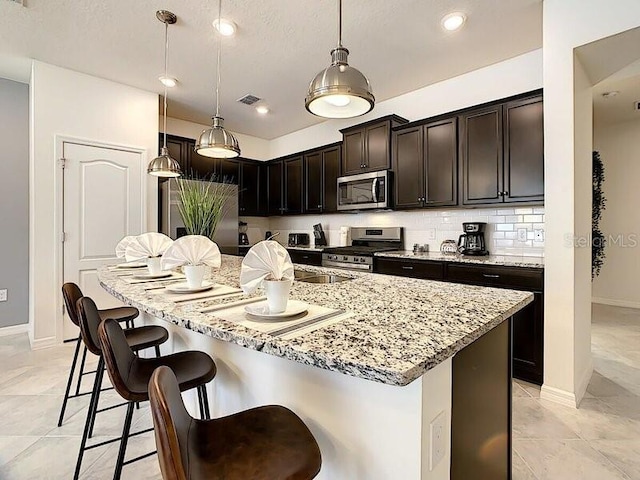 kitchen featuring backsplash, light stone countertops, stainless steel appliances, a breakfast bar area, and a center island with sink