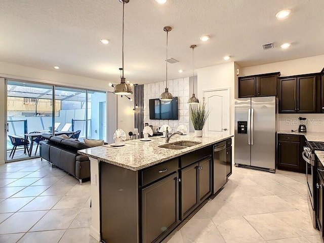 kitchen with a center island with sink, pendant lighting, stainless steel appliances, sink, and light stone counters