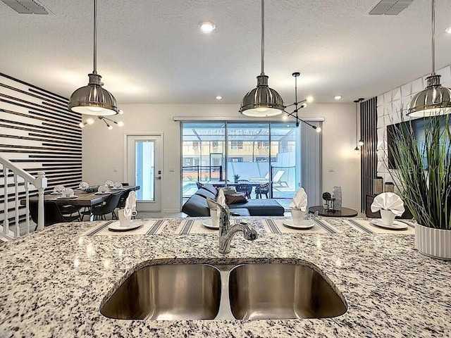 7472 Oakmoss Loop, Davenport, FL 33837 - kitchen featuring a sink, light stone countertops, a textured ceiling, hanging light fixtures, and open floor plan