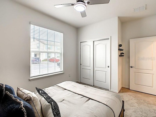 bedroom featuring light colored carpet, ceiling fan, and a closet