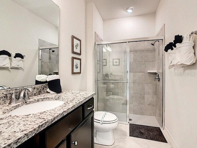 bathroom with a shower with door, vanity, toilet, and tile patterned floors