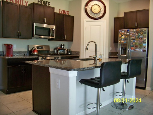 kitchen with light tile patterned floors, sink, appliances with stainless steel finishes, and an island with sink