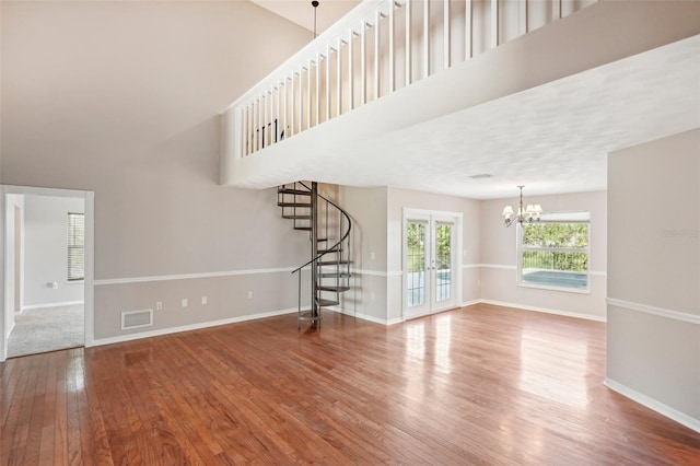 unfurnished living room featuring an inviting chandelier, hardwood / wood-style floors, and a high ceiling