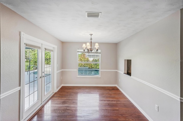 unfurnished dining area featuring an inviting chandelier, wood-type flooring, and french doors