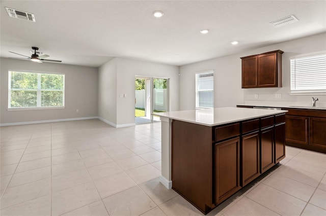 kitchen featuring sink, dark brown cabinets, light tile patterned floors, a center island, and ceiling fan