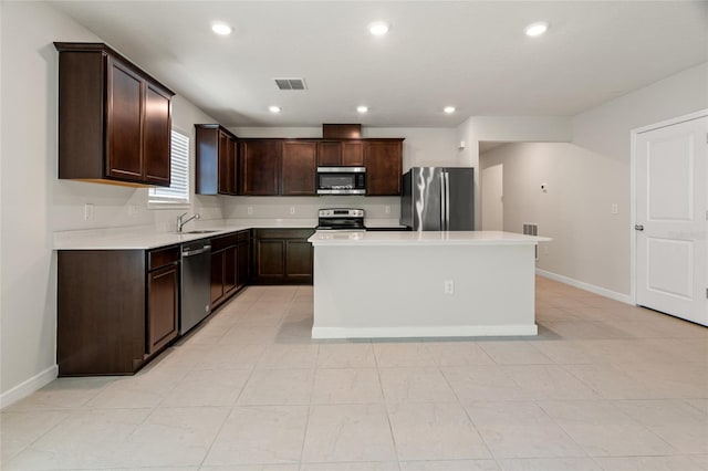 kitchen with appliances with stainless steel finishes, dark brown cabinets, light tile patterned floors, and a kitchen island