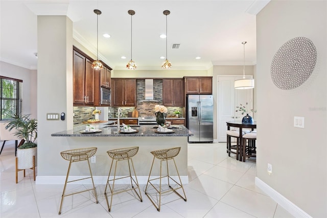 kitchen with wall chimney range hood, decorative light fixtures, dark stone counters, and appliances with stainless steel finishes