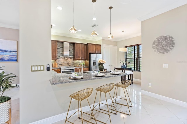 kitchen featuring light stone counters, kitchen peninsula, pendant lighting, stainless steel appliances, and wall chimney range hood