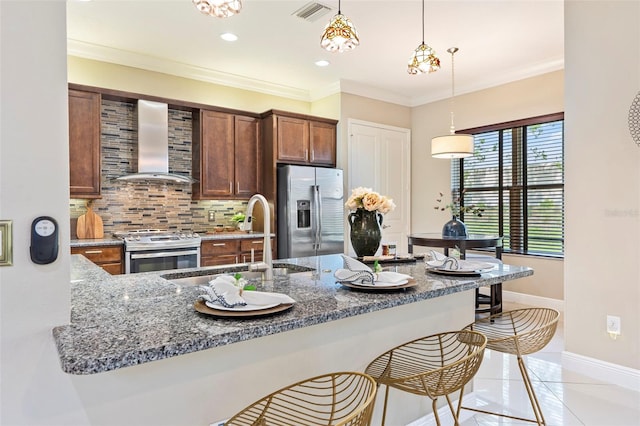 kitchen with sink, decorative light fixtures, appliances with stainless steel finishes, kitchen peninsula, and wall chimney range hood