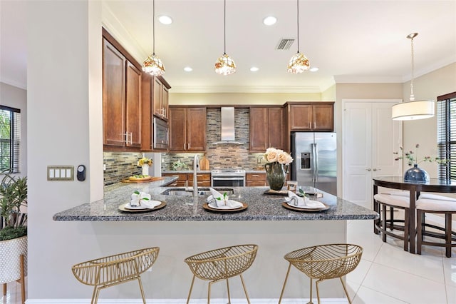 kitchen featuring appliances with stainless steel finishes, hanging light fixtures, a kitchen breakfast bar, kitchen peninsula, and wall chimney exhaust hood