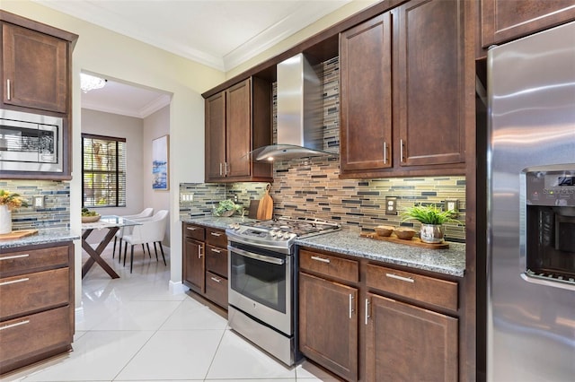 kitchen with appliances with stainless steel finishes, light tile patterned floors, crown molding, light stone countertops, and wall chimney range hood