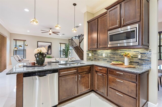 kitchen with appliances with stainless steel finishes, sink, hanging light fixtures, kitchen peninsula, and light stone countertops