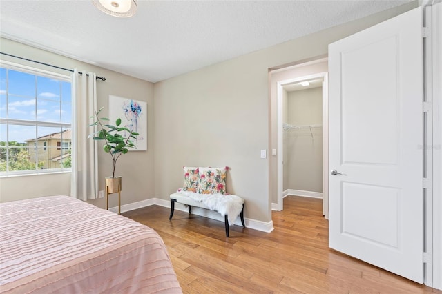 bedroom featuring a walk in closet, a textured ceiling, and light wood-type flooring