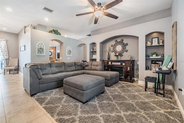 living room with built in shelves, tile patterned floors, a fireplace, and ceiling fan