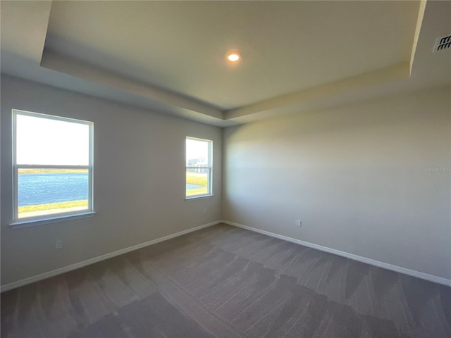 carpeted empty room featuring a water view and a tray ceiling