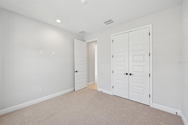 unfurnished bedroom featuring light carpet, a closet, and a textured ceiling