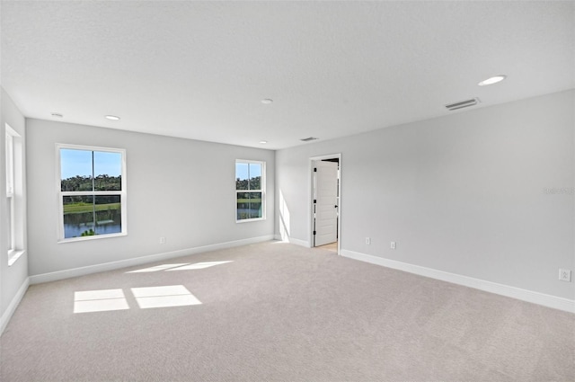 spare room featuring a water view, plenty of natural light, light colored carpet, and a textured ceiling