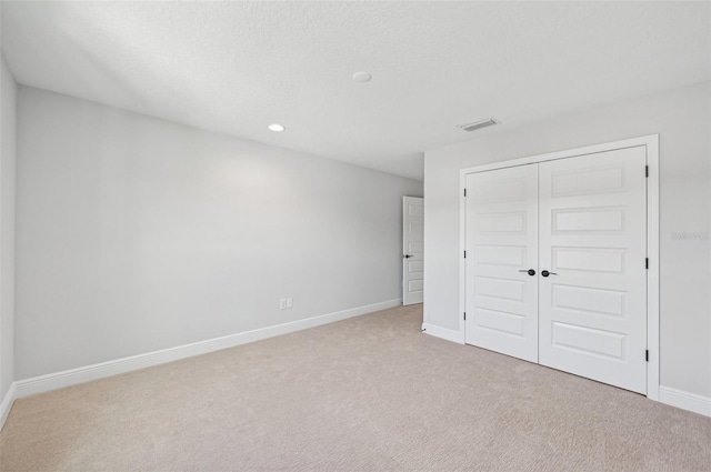 unfurnished bedroom featuring light colored carpet, a closet, and a textured ceiling