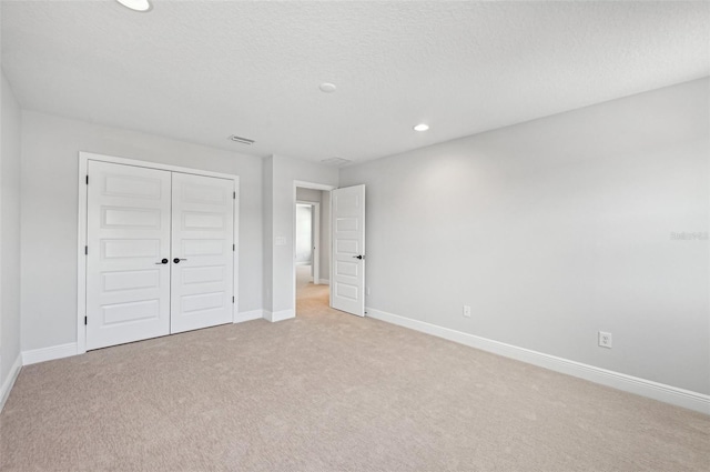 unfurnished bedroom featuring light carpet, a textured ceiling, and a closet