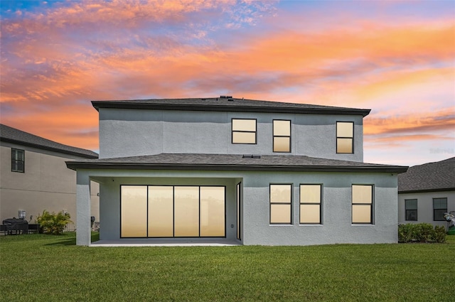 back house at dusk featuring a lawn and a patio area