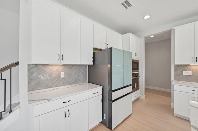 kitchen featuring backsplash, light hardwood / wood-style floors, white cabinets, and appliances with stainless steel finishes