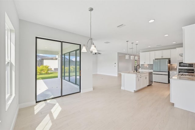 kitchen with white cabinetry, stainless steel appliances, tasteful backsplash, a center island with sink, and decorative light fixtures