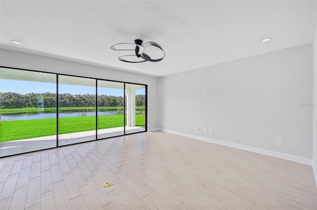 spare room with ceiling fan, a water view, a textured ceiling, and light hardwood / wood-style flooring