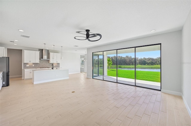 unfurnished living room with a textured ceiling, light wood-type flooring, ceiling fan, and a water view