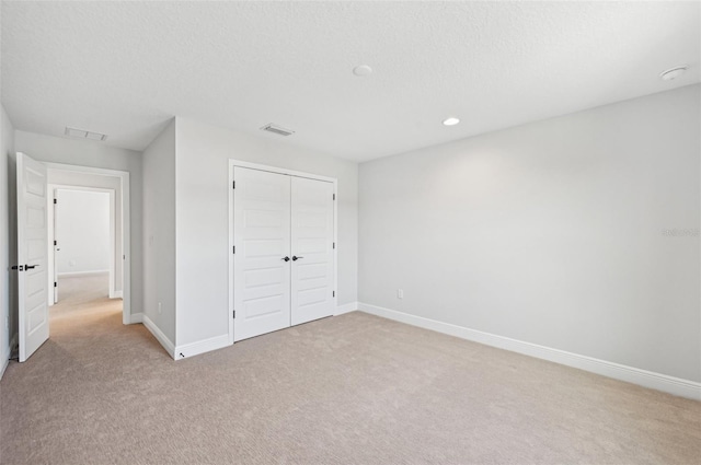 unfurnished bedroom featuring light carpet, a textured ceiling, and a closet