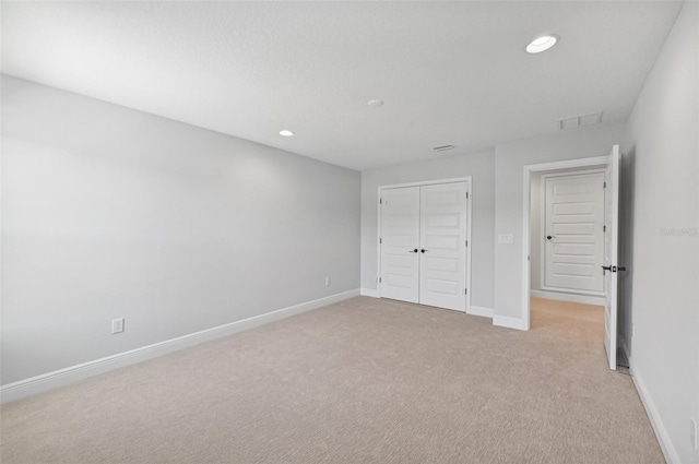 unfurnished bedroom with light colored carpet and a closet