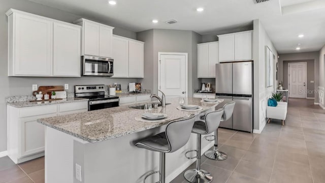 kitchen with white cabinetry, stainless steel appliances, sink, and a center island with sink