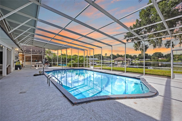 pool at dusk featuring glass enclosure, a water view, and a patio