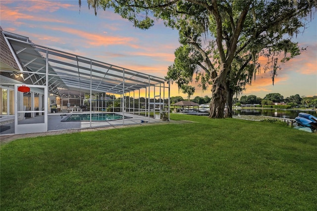 yard at dusk featuring glass enclosure and a water view