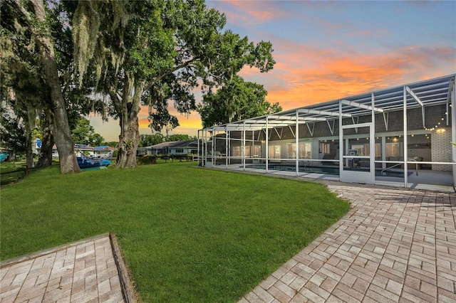 yard at dusk with a pool, glass enclosure, and a patio area