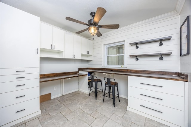 kitchen with white cabinetry, ceiling fan, crown molding, and built in desk